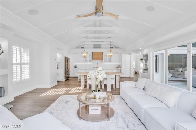 living room featuring ceiling fan, light wood-style flooring, baseboards, and vaulted ceiling