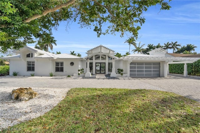 view of front facade featuring decorative driveway, stucco siding, an attached garage, metal roof, and a pergola