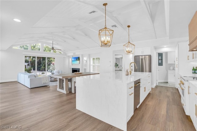 kitchen featuring a fireplace, stainless steel appliances, lofted ceiling, open floor plan, and wood finished floors