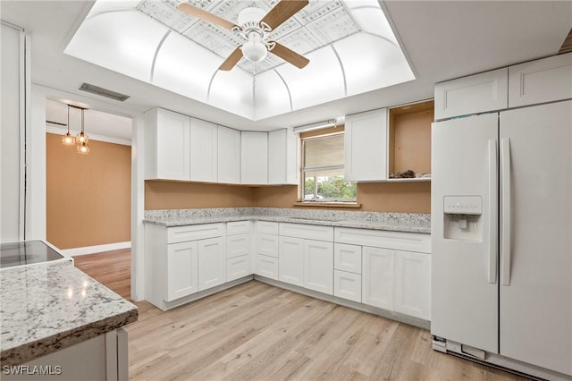 kitchen featuring white refrigerator with ice dispenser, a raised ceiling, light wood-style flooring, a ceiling fan, and white cabinets