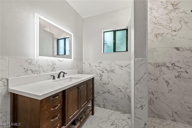 full bath with tiled shower, a wainscoted wall, marble finish floor, vanity, and tile walls