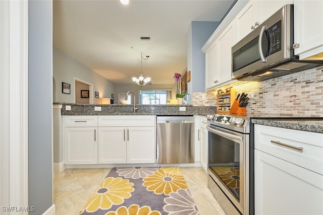 kitchen with appliances with stainless steel finishes, white cabinetry, an inviting chandelier, and tasteful backsplash