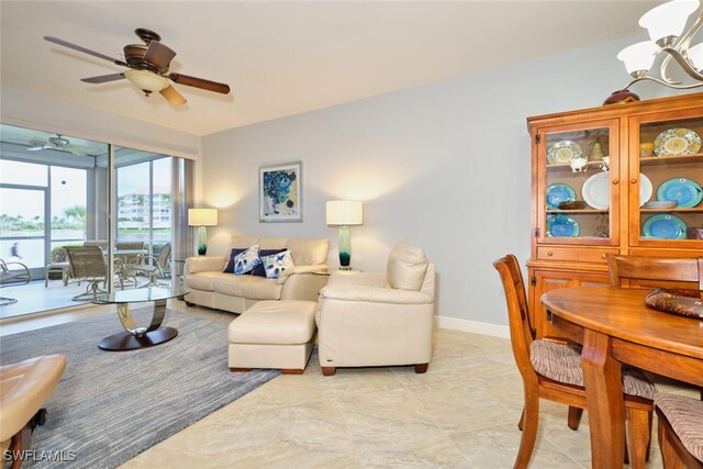 living room featuring ceiling fan with notable chandelier and baseboards