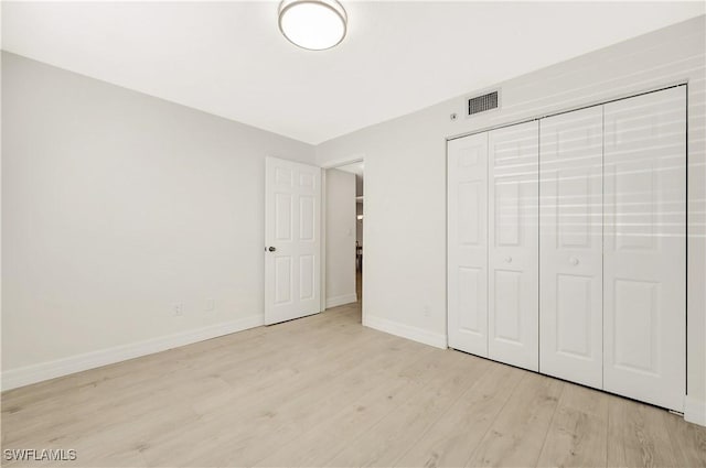 unfurnished bedroom with a closet, wood finished floors, visible vents, and baseboards