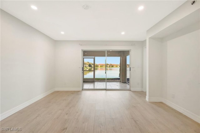 spare room with light wood finished floors, recessed lighting, a water view, and baseboards