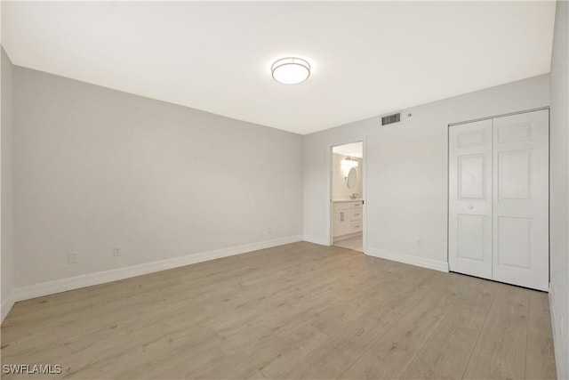 unfurnished bedroom with connected bathroom, visible vents, baseboards, a closet, and light wood finished floors