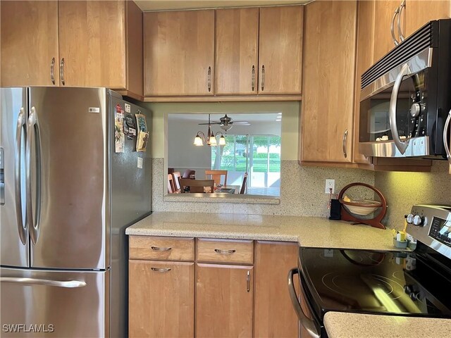 kitchen with brown cabinetry, appliances with stainless steel finishes, light stone countertops, backsplash, and ceiling fan with notable chandelier