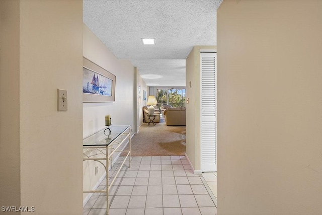 hallway featuring light tile patterned floors, light carpet, a textured ceiling, and baseboards