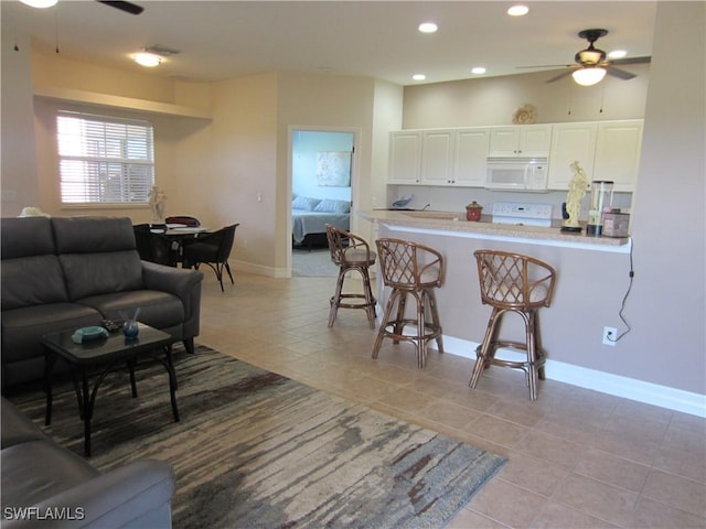 kitchen featuring light tile patterned floors, white microwave, a ceiling fan, white cabinets, and a kitchen bar