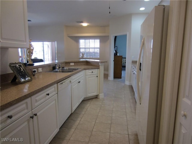 kitchen featuring light tile patterned floors, a peninsula, white appliances, a sink, and white cabinetry