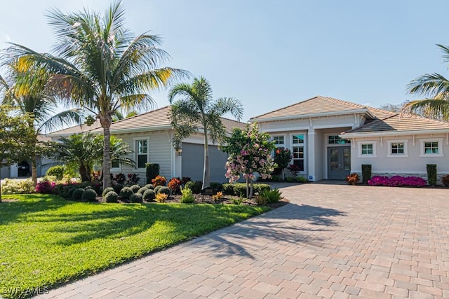 view of front facade with a tile roof, a front lawn, decorative driveway, and french doors