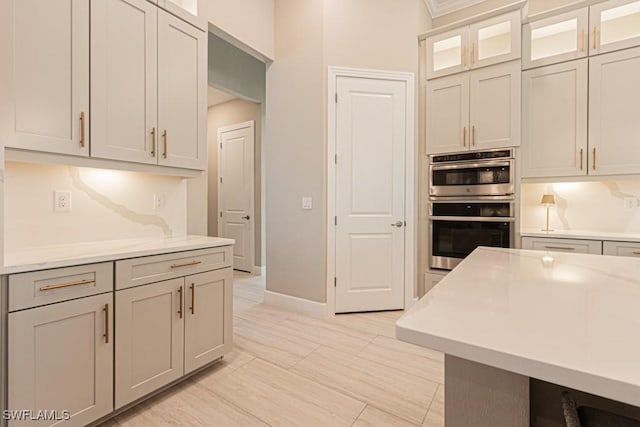 kitchen featuring double oven, light countertops, glass insert cabinets, and baseboards