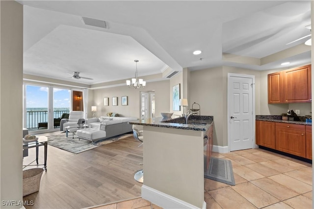 kitchen featuring visible vents, dark stone counters, a raised ceiling, open floor plan, and a peninsula