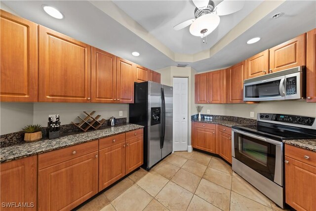 kitchen featuring recessed lighting, dark stone countertops, a tray ceiling, stainless steel appliances, and light tile patterned flooring