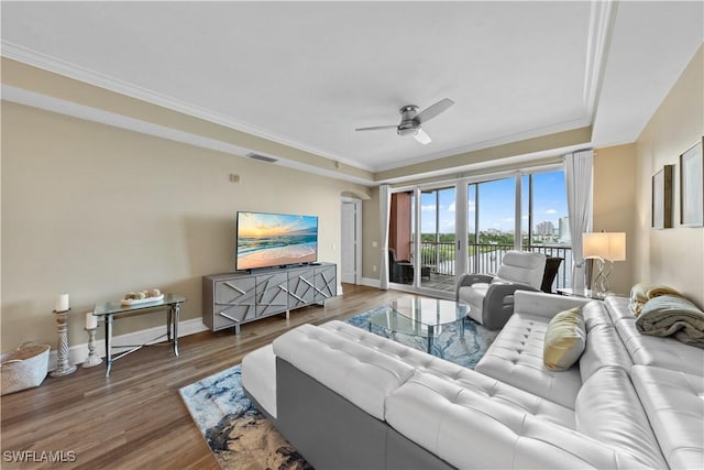 living room featuring ceiling fan, wood finished floors, visible vents, baseboards, and crown molding