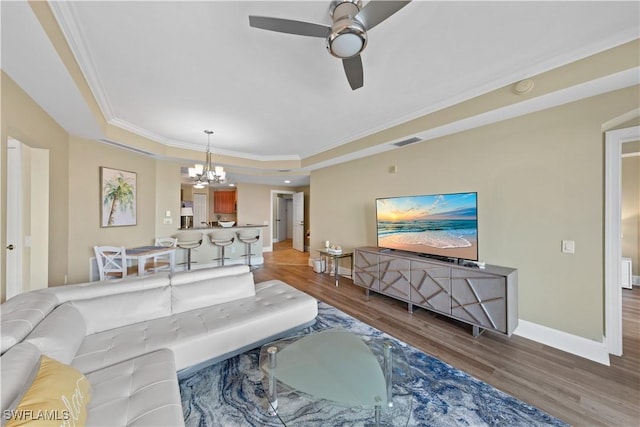 living area with a tray ceiling, visible vents, ornamental molding, wood finished floors, and baseboards