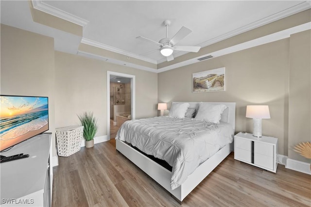 bedroom with wood finished floors, visible vents, baseboards, ornamental molding, and a tray ceiling