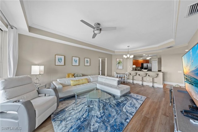 living room with visible vents, ceiling fan with notable chandelier, a tray ceiling, and ornamental molding