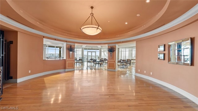 empty room with light wood-style floors, baseboards, a tray ceiling, and crown molding