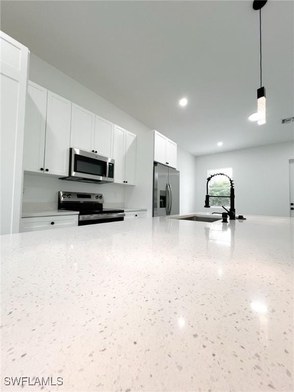 kitchen featuring light stone counters, hanging light fixtures, stainless steel appliances, white cabinetry, and a sink