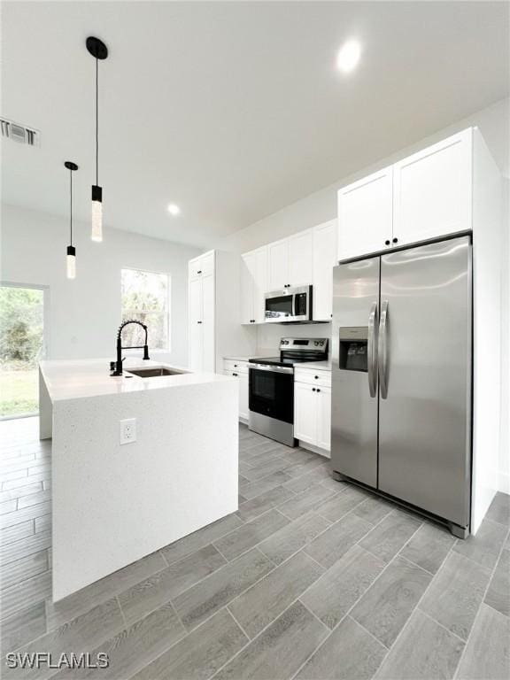 kitchen with stainless steel appliances, a sink, visible vents, white cabinetry, and pendant lighting