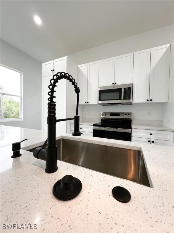 kitchen with stainless steel appliances, light stone counters, and white cabinets