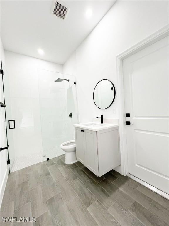 bathroom with visible vents, toilet, wood finished floors, walk in shower, and vanity