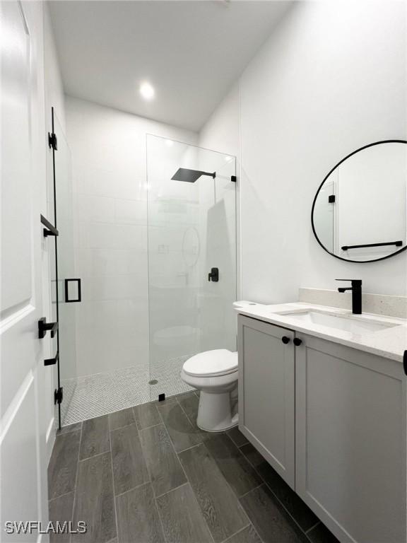 bathroom featuring toilet, wood finish floors, a shower stall, and vanity