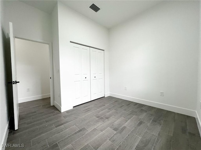 unfurnished bedroom with visible vents, a closet, baseboards, and dark wood-type flooring