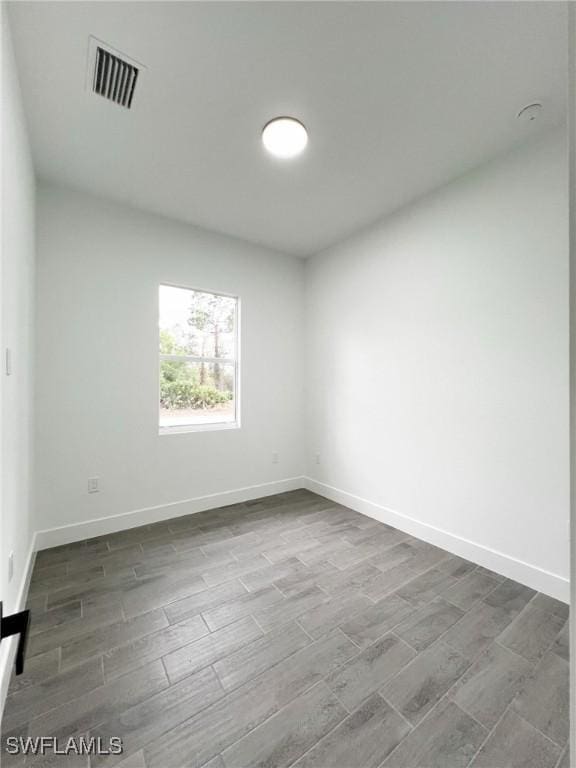 spare room with baseboards, visible vents, and wood finish floors