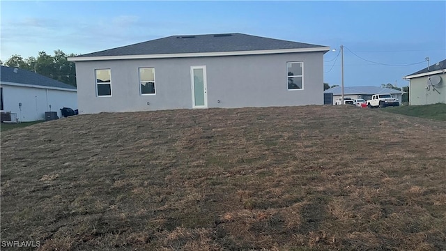 rear view of property featuring central air condition unit, a lawn, and stucco siding