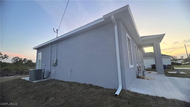 property exterior at dusk featuring central AC and stucco siding