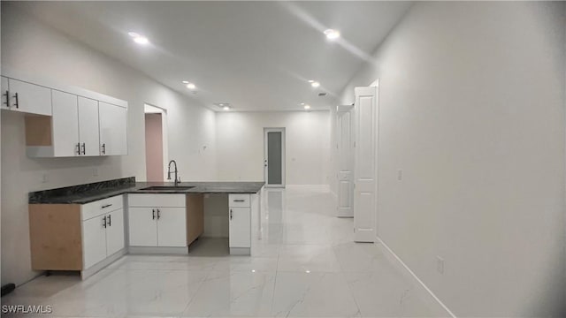 kitchen featuring dark countertops, a peninsula, marble finish floor, white cabinetry, and a sink