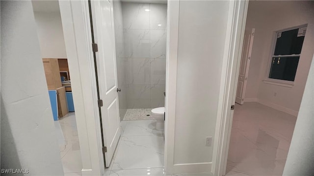 bathroom featuring toilet, marble finish floor, a shower stall, and baseboards