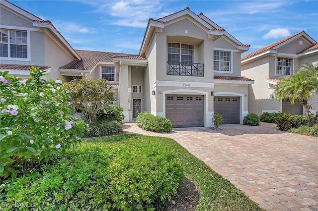 mediterranean / spanish-style home with an attached garage, stucco siding, decorative driveway, and a tiled roof