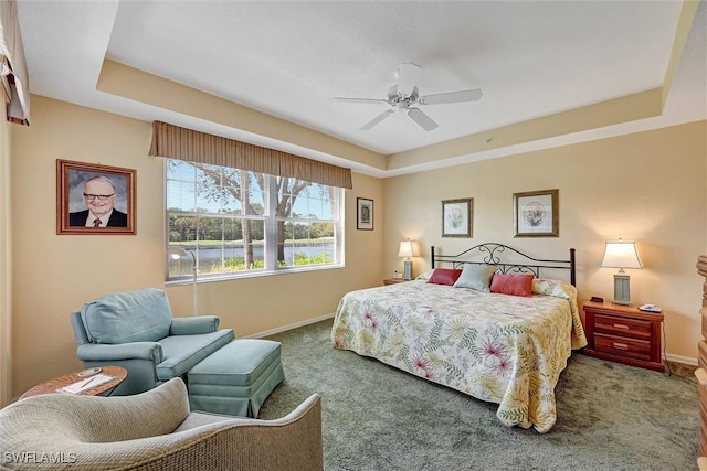 bedroom featuring carpet floors, a water view, a raised ceiling, and baseboards