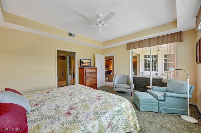 carpeted bedroom featuring visible vents, a raised ceiling, and a ceiling fan