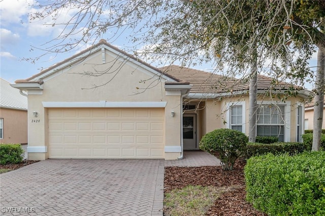 single story home featuring decorative driveway, an attached garage, a tile roof, and stucco siding