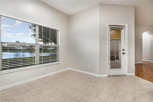 unfurnished room featuring arched walkways, tile patterned flooring, and baseboards