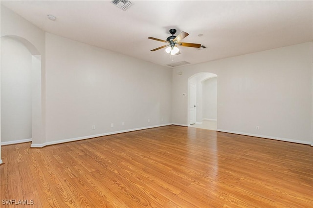 spare room with baseboards, visible vents, arched walkways, a ceiling fan, and light wood-style flooring