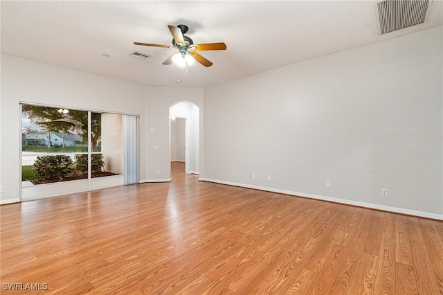 empty room featuring arched walkways, light wood finished floors, visible vents, ceiling fan, and baseboards