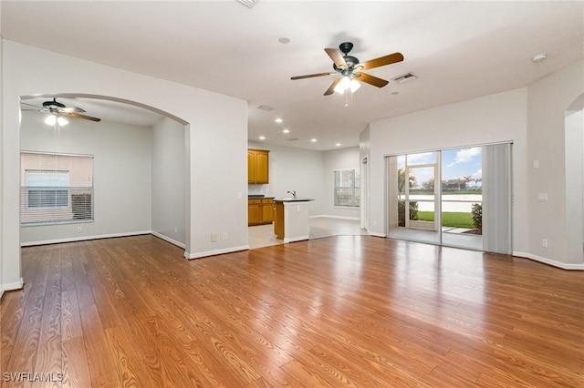 unfurnished living room featuring arched walkways, visible vents, ceiling fan, and light wood finished floors