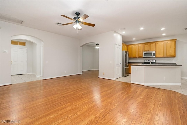 interior space featuring light wood-style floors, ceiling fan, arched walkways, and recessed lighting