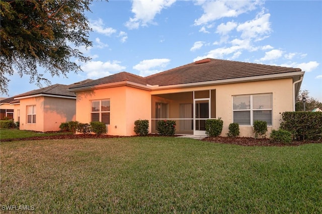 rear view of property with a tile roof, a yard, and stucco siding