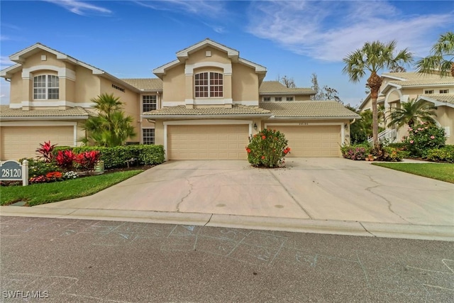 mediterranean / spanish house with driveway, an attached garage, a tiled roof, and stucco siding