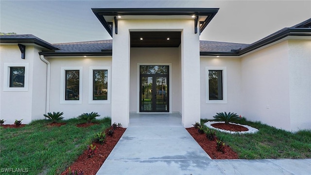 entrance to property with a yard, roof with shingles, and stucco siding