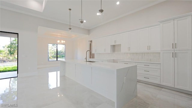 kitchen with a sink, white cabinetry, marble finish floor, decorative backsplash, and a center island with sink