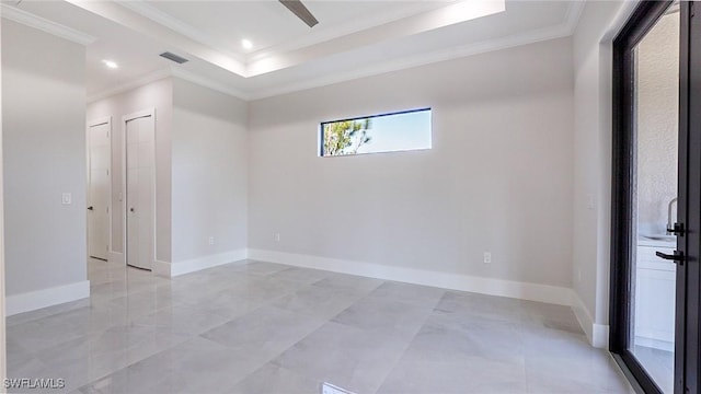 empty room with a tray ceiling, visible vents, crown molding, and baseboards