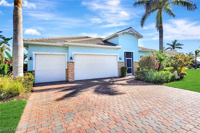 view of front of home featuring an attached garage, stone siding, decorative driveway, and stucco siding