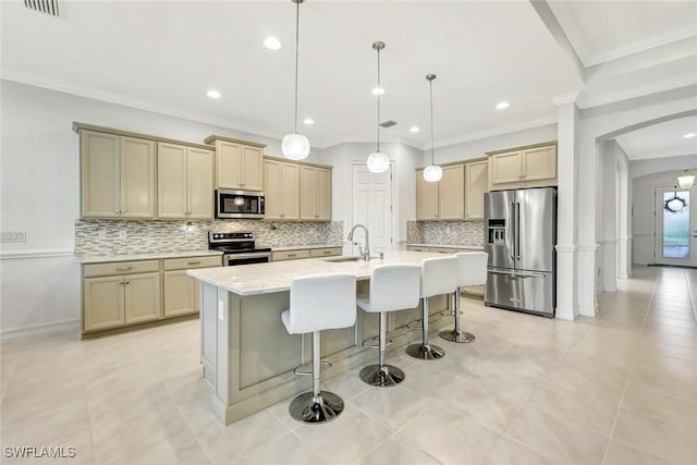 kitchen with arched walkways, a breakfast bar area, stainless steel appliances, decorative backsplash, and an island with sink